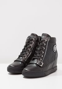 Black wedge sneakers with faux leather and textured side panels, featuring laces, buckle strap, logo detail, and rubber soles.