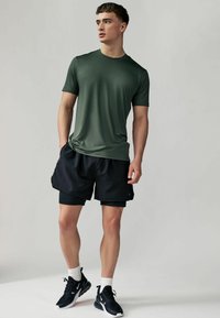Grøn kortærmet trænings t-shirt parret med sorte shorts. Fodtøjet omfatter sorte sportssko og hvide sokker. Simpelt design, åndbart stof.
