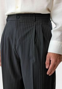 Zwarte pinstripe broek met een getailleerde pasvorm, voorzien van voorpijpen, een knoopsluiting en een gladde stoftextuur.