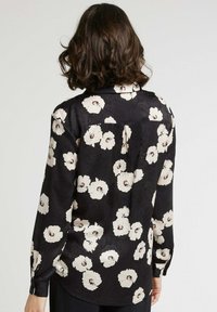 Chemise florale noire avec de grands motifs de coquelicot blancs et des accents roses subtils. Manches longues, col classique et texture lisse.