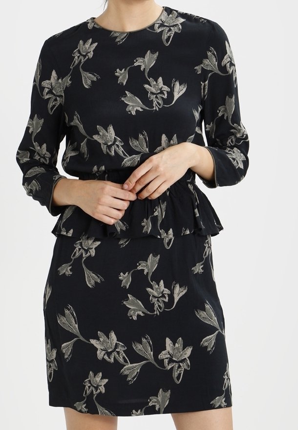 Svart klänning med långa ärmar, prydd med silver blommönster, rund halsringning och volangmidja. Slät textur, ovan knä-längd.