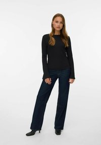 Czarna, długosleeveowa bluzka o teksturowanym wykończeniu, zestawiona z ciemnoniebieskimi dżinsami w szerokim kroju oraz czarnymi botkami na obcasie, z okrągłym dekoltem i dopasowanym fasonem.