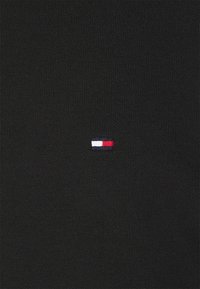 Tessuto nero a maglia con un piccolo logo ricamato dettagliato in rosso, bianco e blu. La texture è liscia con un motivo a coste.