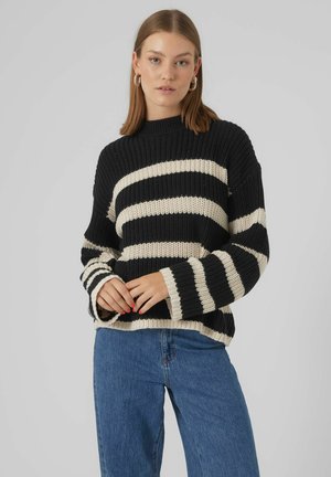Schwarz-weiß gestreifter Strickpullover mit hohem Kragen, lockerer Passform und weiten Ärmeln, kombiniert mit blauen Jeans.