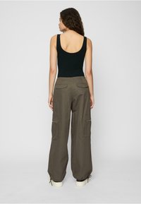 Black tank top and olive green cargo pants with two back pockets, side pockets, and zippered accents. Loose fit with adjustable cuffs.