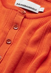 Gros plan sur un cardigan en maille côtelée orange avec des boutons assortis et une étiquette de marque ARMENDANGELS blanche à l'intérieur du col.