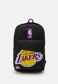 Le sac à dos en tissu noir présente le logo de la NBA et "Los Angeles Lakers" en violet sur un graphique de ballon de basket jaune. Des accents de fermeture éclair violets sont inclus.
