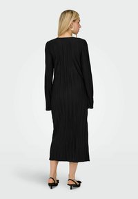 Svart veckad klänning med långa ärmar, slim fit och knälång längd. Har rund halsringning och texturerad tyg för visuell djup.