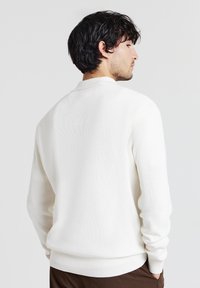 Weißer gerippter Strickpullover mit lockerer Passform, rundem Kragen und langen Ärmeln. Die Ärmel und der Saum haben eine gerippte Textur für zusätzliche Details.