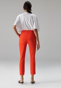 Witte oversized T-shirt met korte mouwen gecombineerd met nauwsluitende, felrode broek tot aan de enkels en zwarte sloffen met hak. Overal gladde texturen.