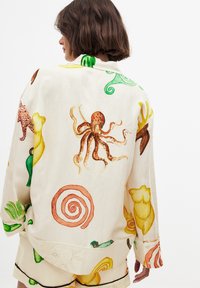 Linnen skjorta med färgglada djur- och spiral mönster, med en avslappnad passform och gröna detaljer vid kragen.