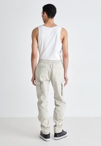 Helle beige Cargo-Hosen mit Seitentaschen, elastischem Bund und lockerer Passform. Getragen mit einem weißen Tanktop und schwarzen Sneakers.