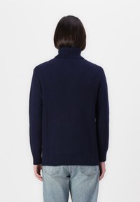 Dunkelblaues geripptes Rollkragensweatshirt mit langen Ärmeln, das ein strukturiertes Strickdesign aufweist. Trägt dazu hellblaue Jeans.