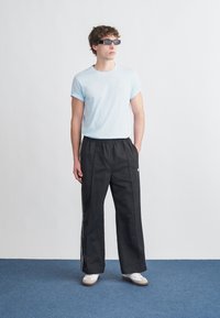 Ανοιχτό γαλάζιο κοντομάνικο μπλουζάκι, μαύρο παντελόνι με φαρδιά μπατζάκια και λευκές ρίγες στα πλάγια, και λευκά αθλητικά παπούτσια. Αξεσουάρ: σκούρα ορθογώνια γυαλιά ηλίου.