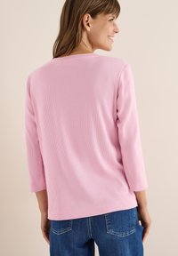 Lys rosa, ribbet langærmet top med lige snit og dropped shoulder-design, parret med blå denim jeans.