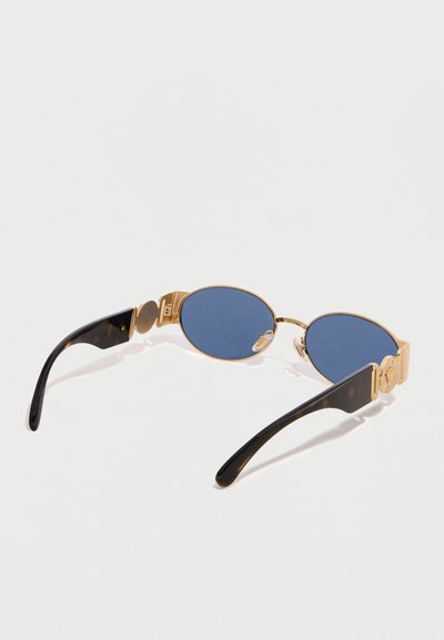 Οβάλ γυαλιά ηλίου με μπλε φακούς και χρυσό μεταλλικό σκελετό, με λεπτομερείς χρυσές λεπτομέρειες στα μαύρα βραχίονες από χελώνα, εμφανιζόμενα σε λευκό φόντο.