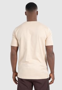 Beige katoenen t-shirt met korte mouwen, voorzien van een ronde halslijn en een zachte textuur, weergegeven van de achterkant, gecombineerd met donkere broek.