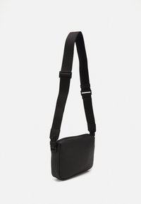 Černá krosová taška s texturovaným koženým vnějším povrchem, nastaviteln�ým nylonovým popruhem a obdélníkovým tvarem. Jednoduchý design, žádné viditelné kování.