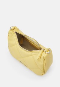 Żółta skórzana torebka z pikowanym wzorem, srebrnym zamkiem błyskawicznym i zaokrąglonym kształtem. Wnętrze ma gładką teksturę, ukazując przestrzeń do przechowywania.