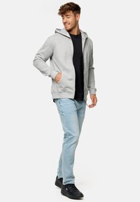 Grå zip-up hoodie med snøre hætte, parret med en sort t-shirt, lyseblå jeans og sorte sneakers. Har sidelommer.