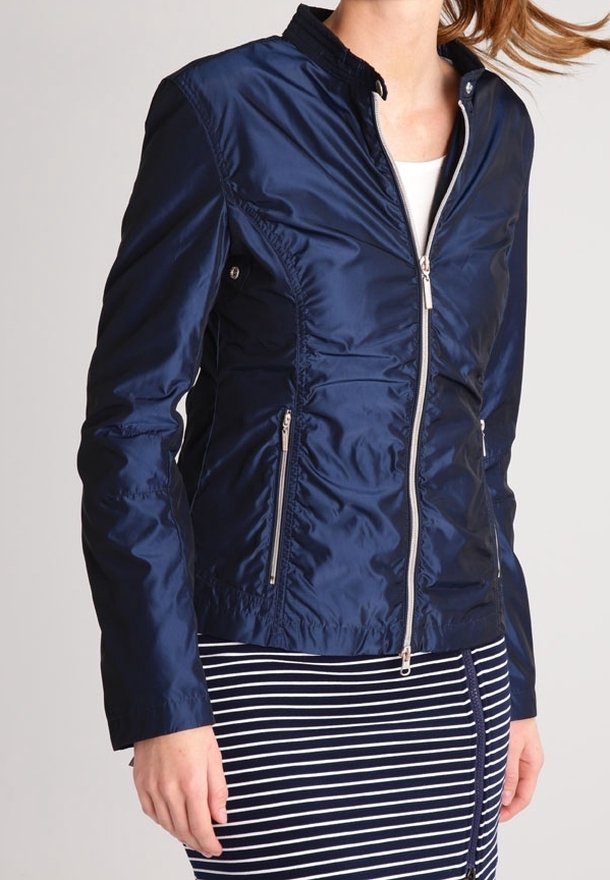 Navy blue nylon jacket with a fitted design, collar, side pockets, and silver zipper accents. Worn with a striped skirt.