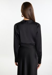 Abito in satin nero con maniche lunghe e colletto, caratterizzato da una texture liscia e una vita con cintura. Design elegante e minimalista.