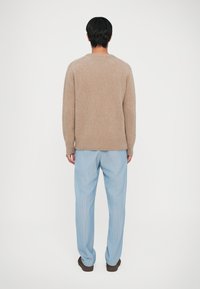 Kreminė megzta džemperis su laisvu kirpimu ir raštuotais kraštais, derinamas su mėlynomis dryžuotomis kelnėmis. Komplektas pasižymi švelnia tekstūra ir kasdiene dizainu.