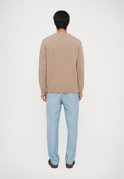 Pull en tricot beige à coupe décontractée et ourlet en côtes, associé à un pantalon rayé bleu. L'ensemble présente une texture douce et un design décontracté.