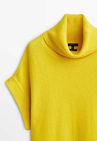 Keltainen neulepusero, jossa on korkea kaulus, lyhyet hihat ja ribbikuvio. Pehmeä materiaali, jossa on sileä pinta.