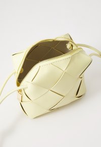 Yellow woven leather bag with a zip closure, featuring a smooth texture and soft, rounded edges. Interior is beige with a structured design.