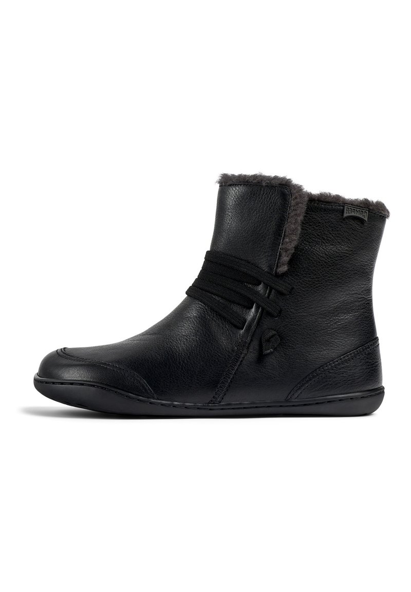 Botas de tobillo de cuero negro con un suave forro de piel de pelaje gris, que cuentan con bandas elásticas para el cierre y una suela flexible. Diseño simple y estilizado.