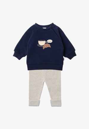 Navyblaues Sweatshirt mit einem Motiv von einer Tasse und einem Croissant, kombiniert mit hellgrauen gerippten Hosen mit umgeschlagenen Knöcheln.