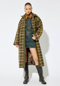 Lång rutig kappa i brun och grön ullblandning, med en oversized passform och tryckknappsstängning. Bärs över en denimklänning; knähöga stövlar.