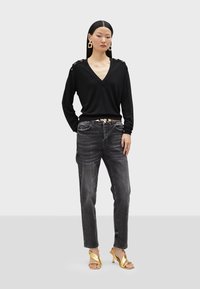 Svart långärmad v-ringad topp med knapppdetaljer på axlarna, kombinerad med urtvättade grå jeans och blanka guldklackar. Enkelt och modernt design.