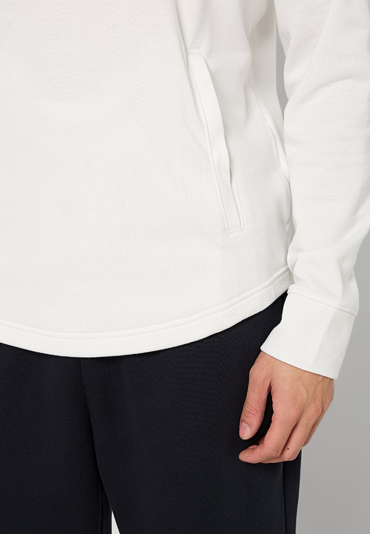 Haut à manches longues blanc au toucher doux, avec des poches latérales et des manches à poignets, associé à un pantalon sombre.