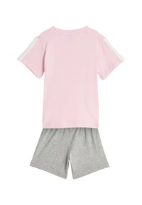 Camiseta de algodón rosa con detalles blancos en las mangas, combinada con pantalones cortos grises. La camiseta tiene un cuello redondo y un ajuste holgado.