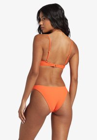 Pomarańczowy bikini z żebrowanym wzorem, z regulowanymi ramiączkami, metalowym zapięciem z tyłu oraz dolną częścią o niskim stanie, z subtelnym detalem logo.