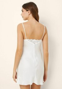 Camisón de satén blanco con finas correas ajustables, adornos de encaje en la espalda, y un diseño suave y fluido.