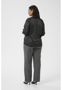 Blouse noire à pois avec manches longues, associée à un pantalon large gris. Texture de tissu lisse ; couleur unie et détails de motif visibles.