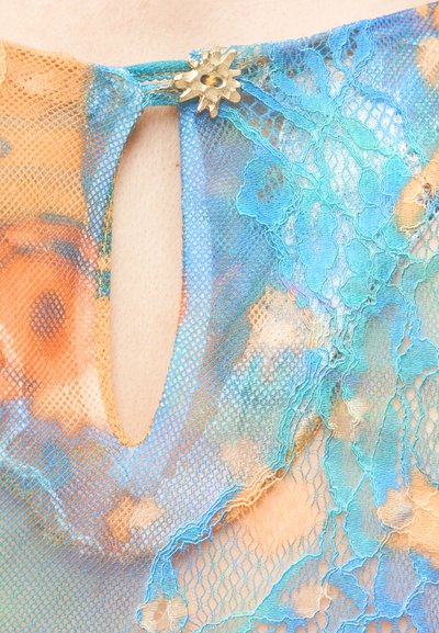 Τοπ από δαντέλα με λαιμόκοψη σε σχήμα κλειδαρότρυπας, ζωηρά πορτοκαλί και μπλε λουλουδένια σχέδια, με χρυσό κούμπωμα σε σχήμα εκλάμψεων στον λαιμό.