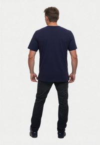 Camiseta de manga corta azul marino, material de algodón, cuello redondo, corte recto, combinada con pantalones negros y zapatillas oscuras, vista desde la parte posterior.