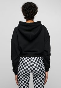 Hoodie nero corto con cappuccio, abbinato a leggings a vita alta con un motivo a scacchi bianco e nero. Tessuto morbido.