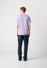 Lys lilla polo skjorte med korte ærmer, vist fra bagsiden, parret med mørkeblå denim jeans og sorte sko. Glat stof tekstur.