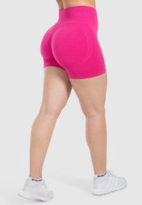 Fuchsia hoge taille compressiekorte broeken met een naadloos ontwerp, rekbare stof en contourdetails, gecombineerd met witte sportschoenen.