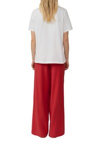 T-shirt en coton blanc à manches courtes, associé à un pantalon large rouge en tissu doux. Coutures visibles en accent.