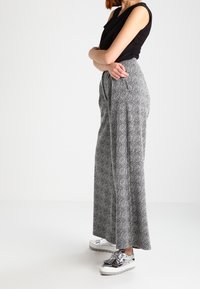 Pantalon à jambes larges à motifs noir et blanc avec une taille haute, associé à des chaussures à plateforme argentées. Tissu lisse et coupe décontractée.