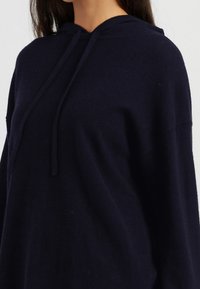 Felpa con cappuccio blu navy realizzata in un tessuto morbido e testurizzato, con una vestibilità comoda e coulisse. Presenta un design minimalista e spalle scese.