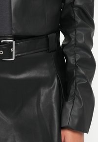 Svart skinnjakke med glatt tekstur, belted midje med sølvfargede detaljer, og rynkede ermer for en strukturert design.