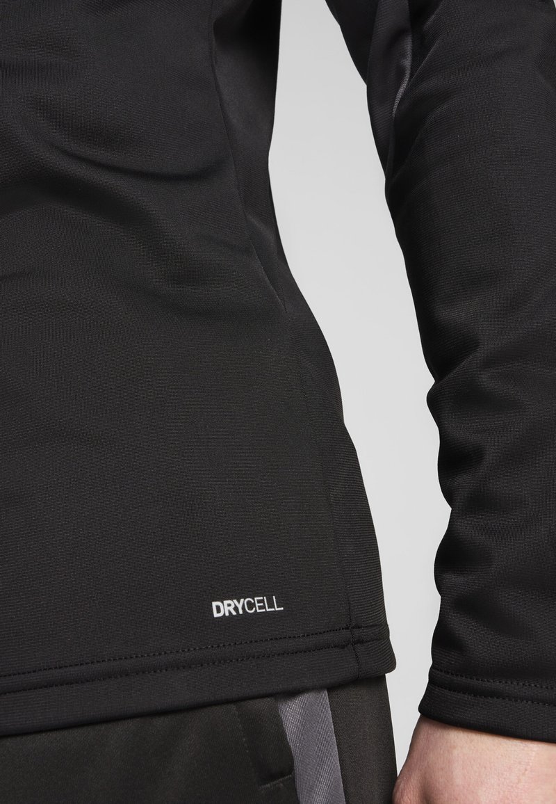 Svart langermet treningstopp med teksturert stoff. Har en hvit "DRYCELL" logo nær sømmen. Nærbilde som fremhever passform og detaljer.
