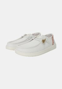 Witte canvas schoenen met een ronde neus, gestructureerde bovenkant en contrasterende stoffen accent op de hiel. Heeft subtiele veters en kwastje-detail.